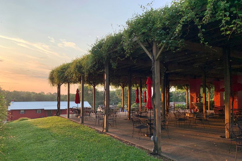 tables on a patio covered in greenery with the sun setting in the background at Augusta Winery