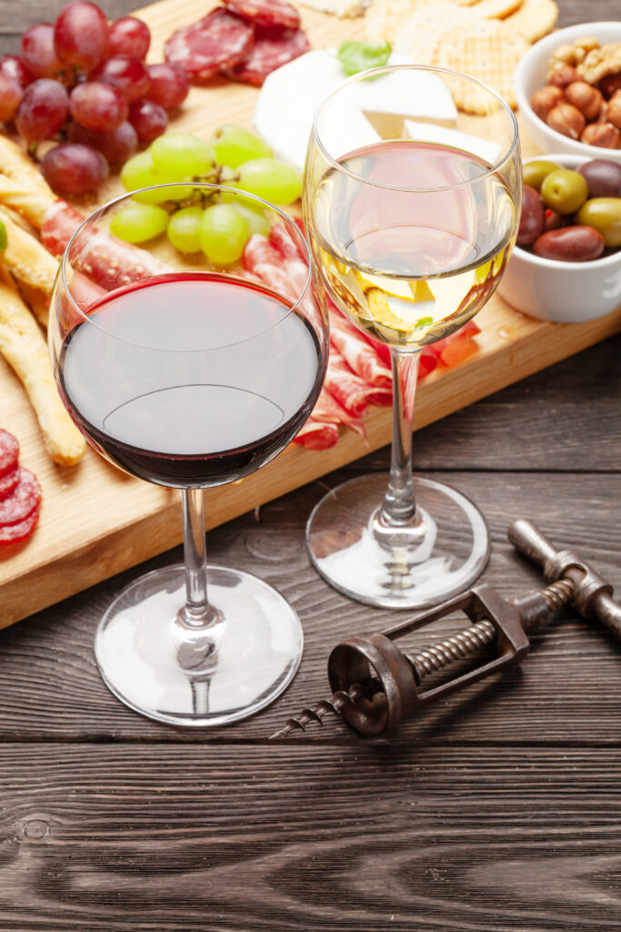 Cheese, meat, grapes and olives antipasto. Appetizer selection on wooden board and glasses with red and white wine